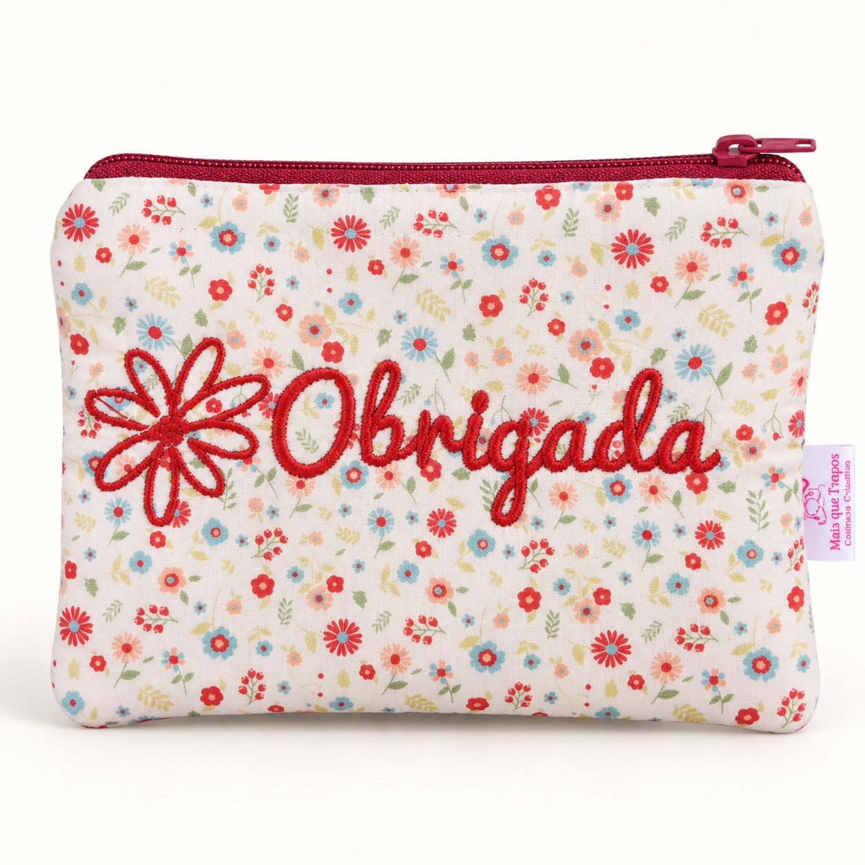 Bolsa bege com flores coloridas e bordado “Obrigada”, zíper vermelho e etiqueta lateral.